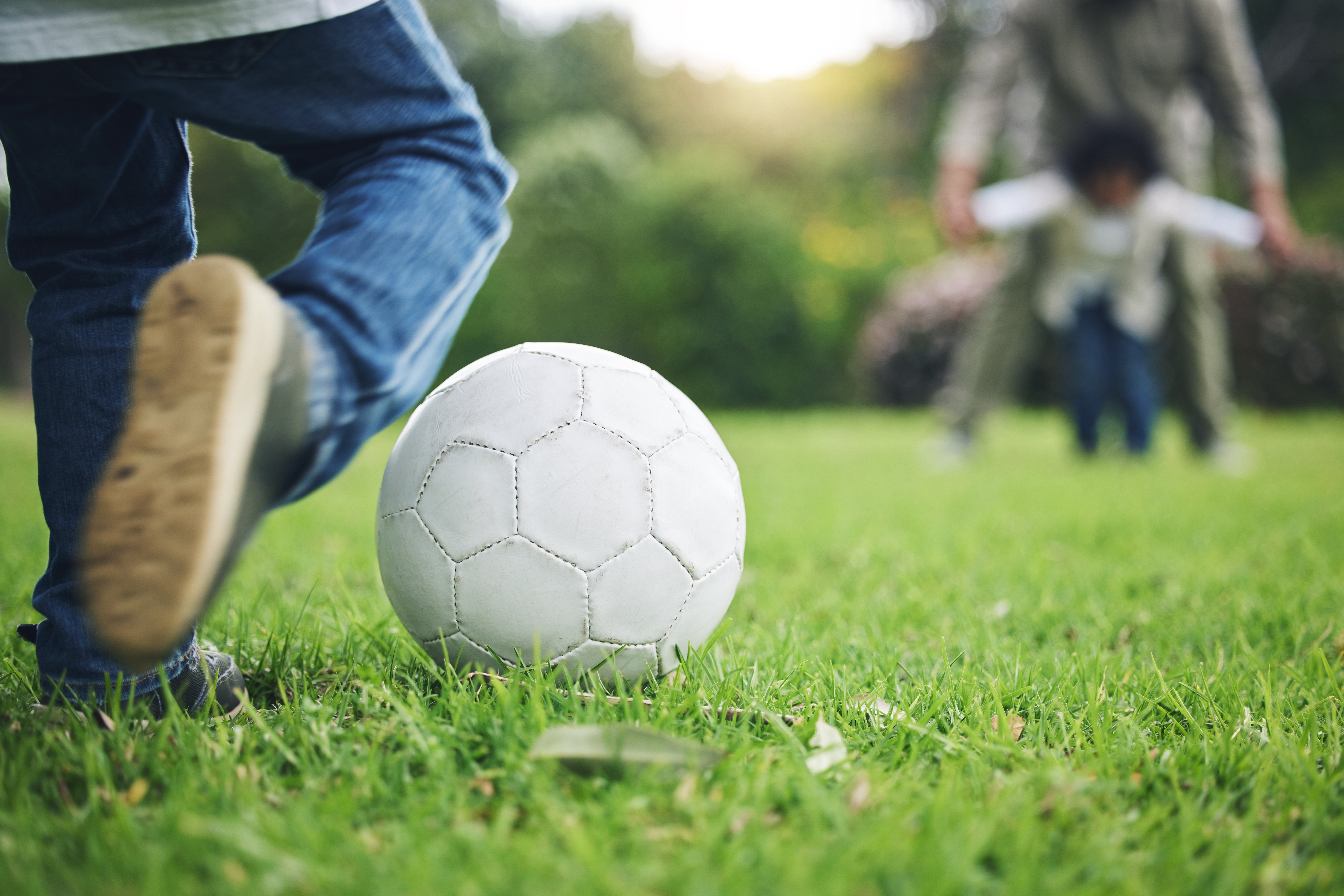 Child, legs and kick soccer ball on grass for fun activity, childhood or playing in the park. Playf.