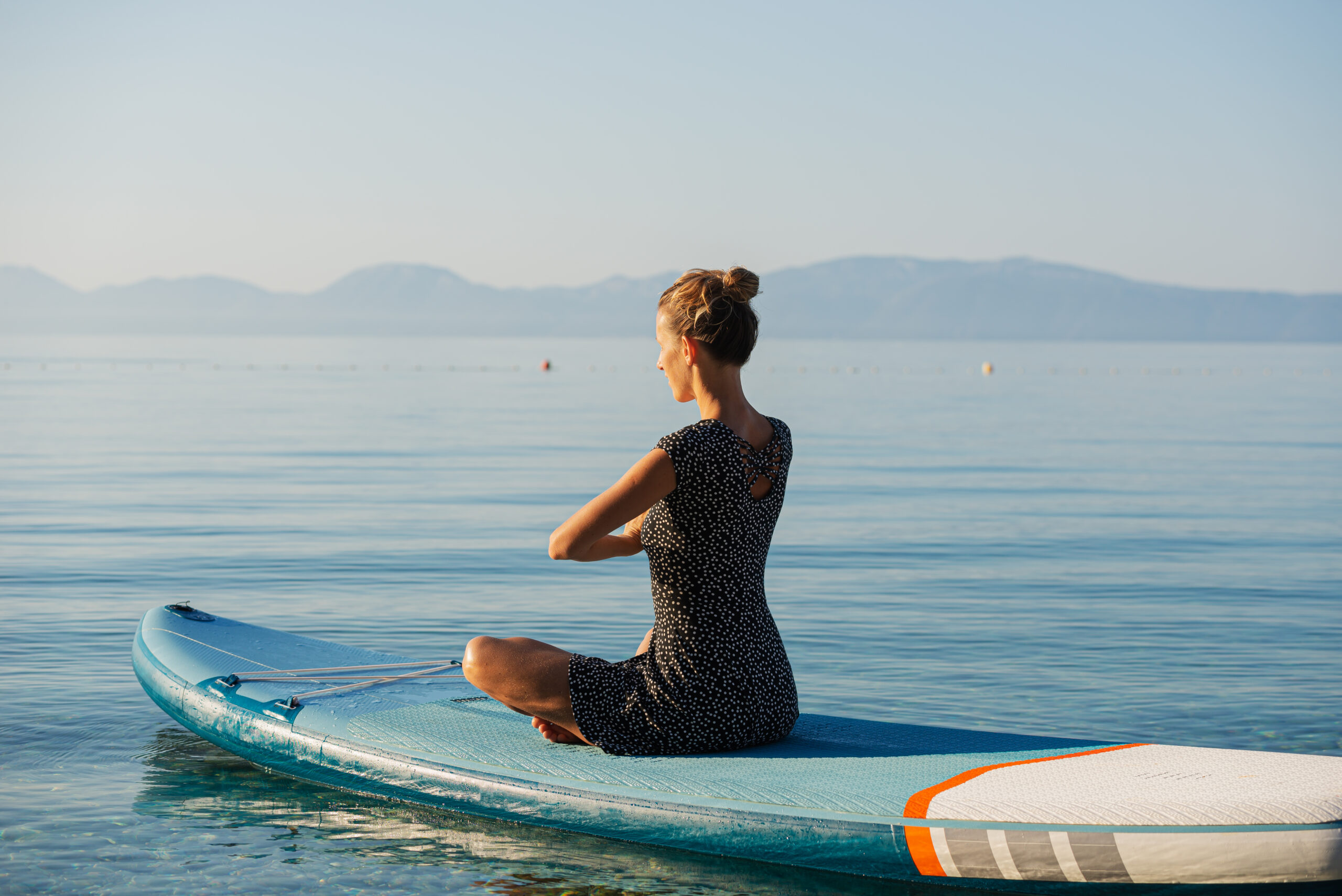 Bodensee Young woman sitting in lotus position meditating on sup board floating on calm morning sea water.