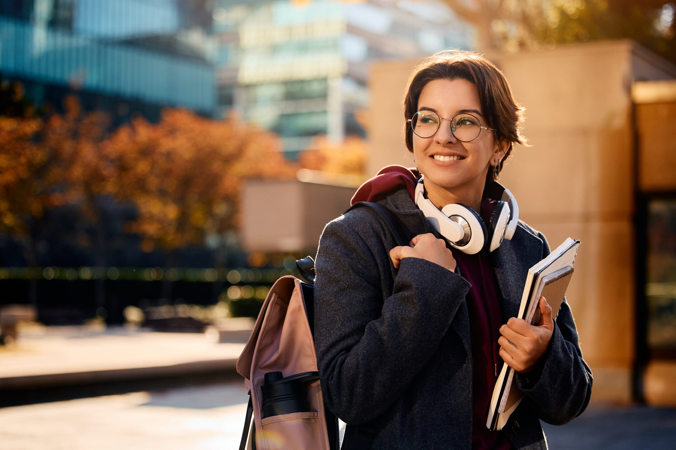 Young happy woman carrying backpack and books while going on a lecture at campus.